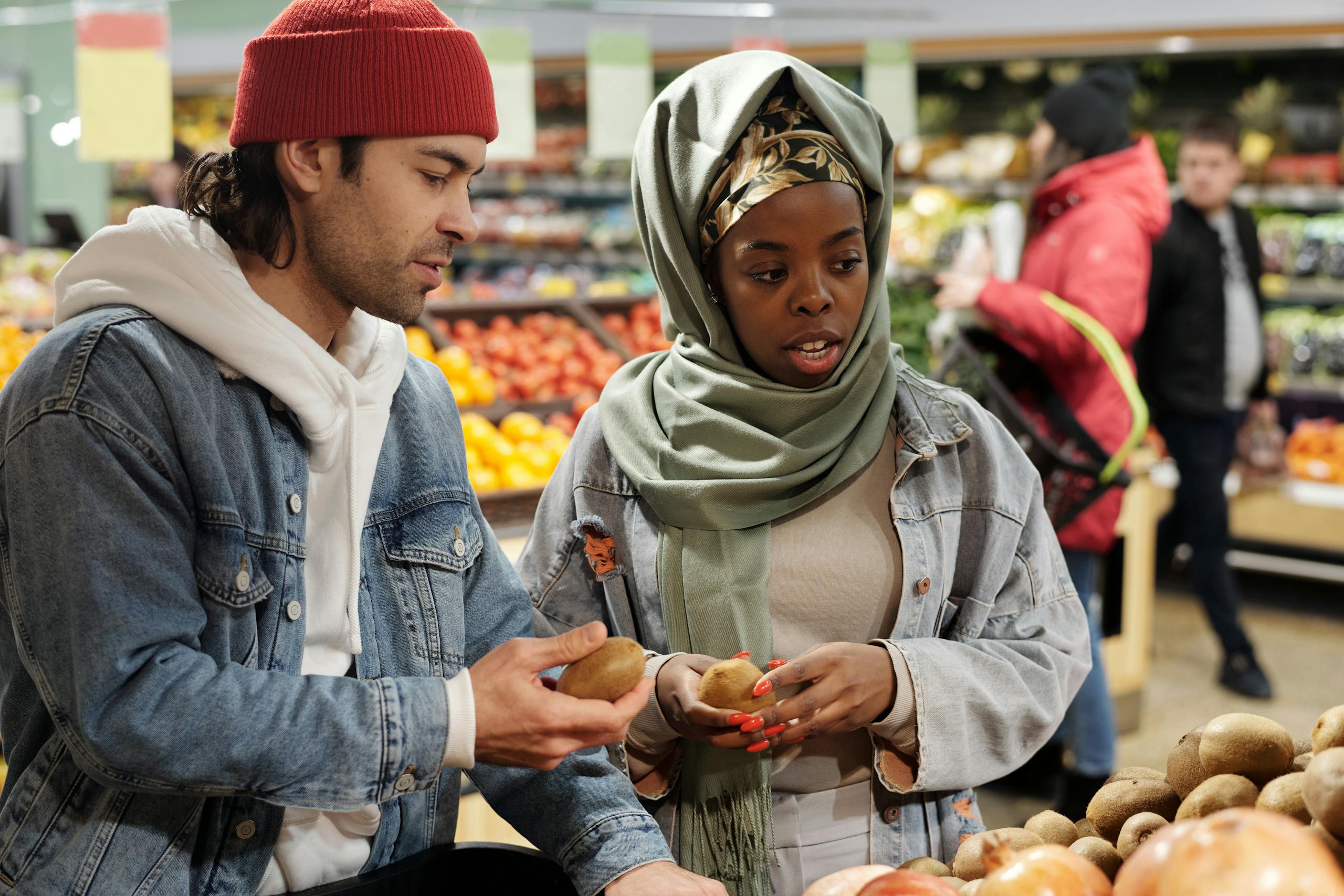 A diverse couple selecting fresh kiwis in a vibrant supermarket produce section.